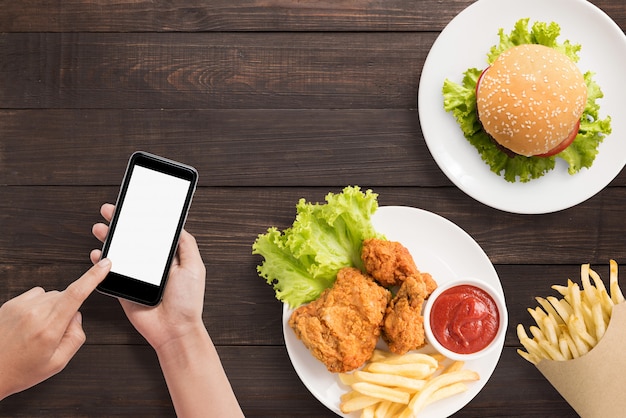 À l'aide de smartphone avec burger, frites et poulet frit sur fond de bois