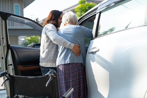 L'aide soignante et le soutien d'une femme âgée asiatique assise sur un fauteuil roulant se préparent à se rendre à sa voiture pour voyager en vacances