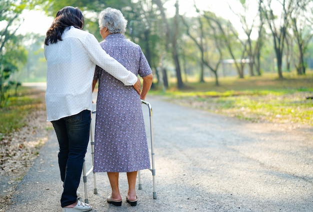 Photo aide et soins une femme senior asiatique utilise une marchette en se promenant dans un parc.