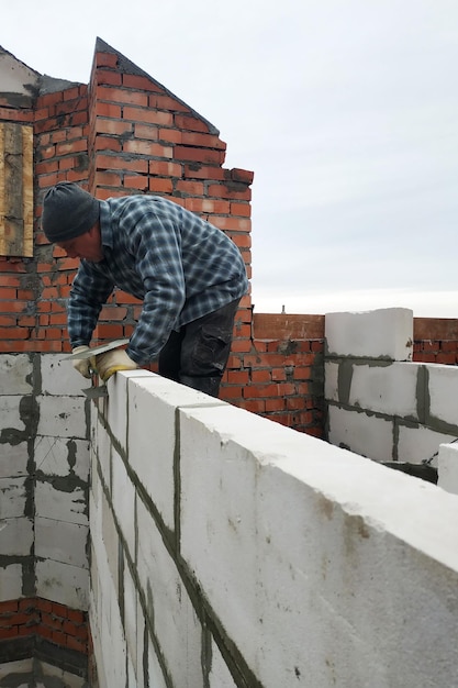 Avec l'aide d'une solution gluante, le travailleur construit un mur de blocs de gaz