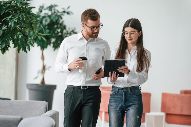 À l'aide d'une tablette numérique, un homme et une femme en vêtements formels travaillent ensemble à l'intérieur