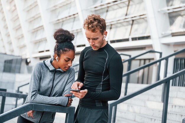 À l'aide de téléphone, un homme européen et une femme afro-américaine en vêtements sportifs s'entraînent ensemble