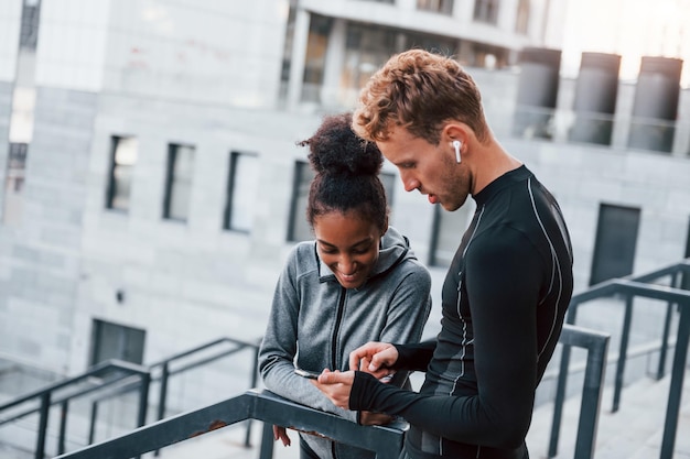 À l'aide de téléphone, un homme européen et une femme afro-américaine en vêtements sportifs s'entraînent ensemble