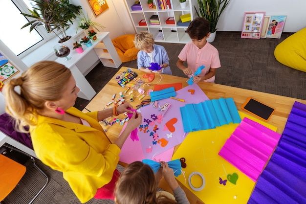 Aider les écoliers. Enseignant en veste jaune aidant les écoliers à faire des découpes et des décorations