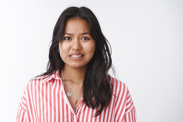 Aïe j'ai des ennuis. Portrait d'une collègue féminine mignonne, insécurisée et troublée, faisant un énorme désordre au travail, serrant les dents maladroitement et désolé d'admettre sa faute en disant oops sur fond blanc