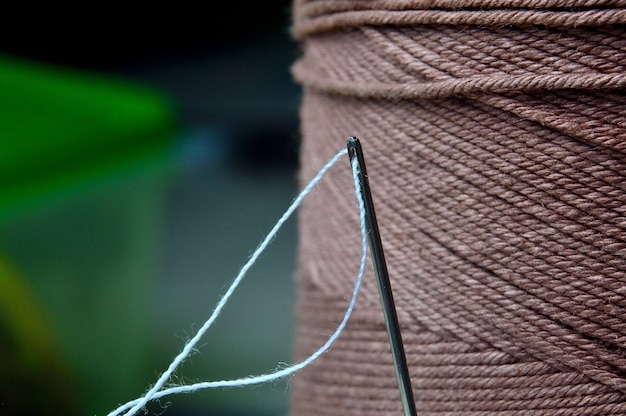 Une aiguille avec un fil inséré dans le fond d'une grande bobine de fil