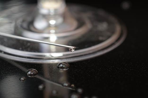 Une aiguille avec une goutte d'eau dessus repose sur une surface noire.