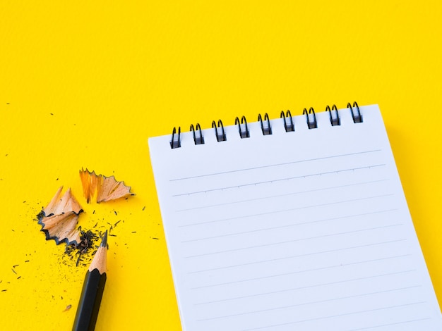 Aiguiser un crayon noir et un carnet de notes sur fond jaune.