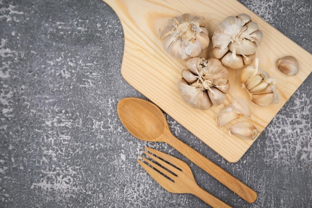 Ail cru frais sur l'affichage de la planche à découper avec fourchette et cuillère sur fond sombre pour la mise en place du concept de cuisine