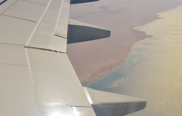 Aile d'un avion de ligne sur fond de mer et de désert.