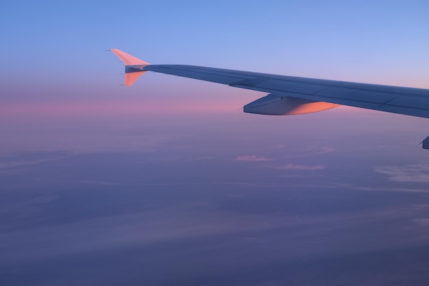 Aile d'avion à travers le hublot dans les rayons du soleil couchant aux couleurs bleues et roses