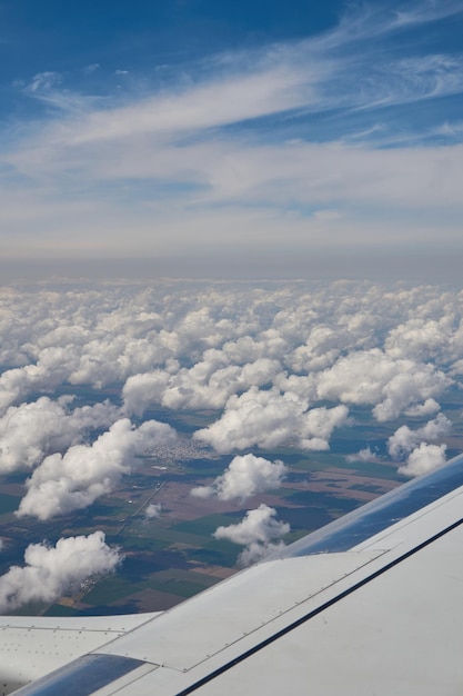 Aile d'un avion volant au-dessus des nuages et des champs verts