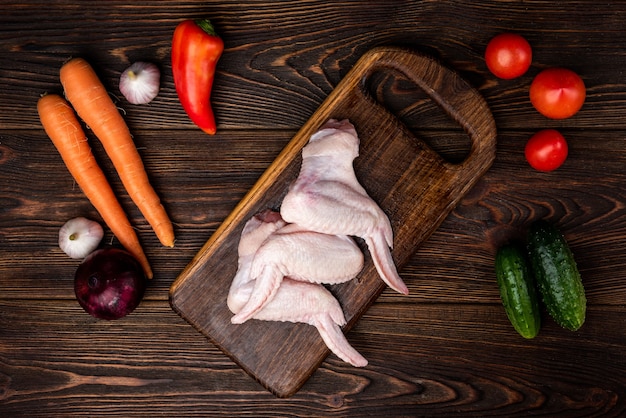 Ailes de poulet cru sur bois foncé avec des légumes.