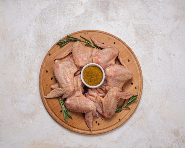 Ailes de poulet crues au romarin et curry sur une planche ronde en bois. Cuisine maison, plats cuisinés. Viande de volaille crue