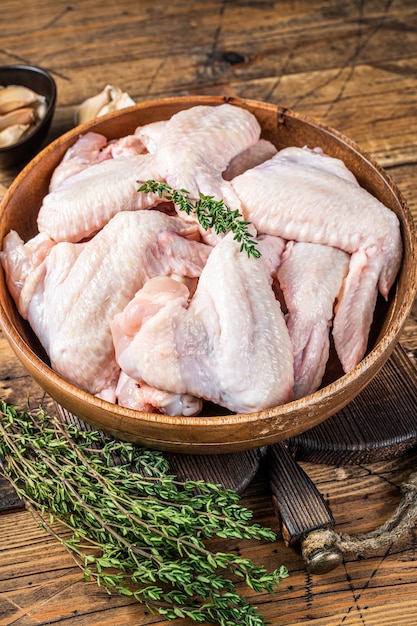 Ailes de poulet crues dans une assiette en bois avec du thym et de l'ail. Fond en bois. Vue de dessus.