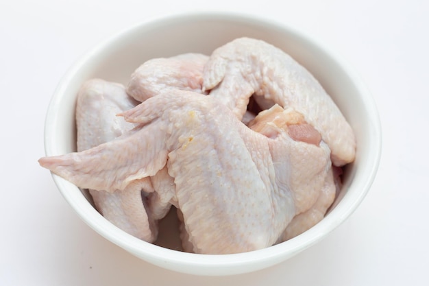 Ailes de poulet crues fraîches dans un bol blanc sur fond blanc