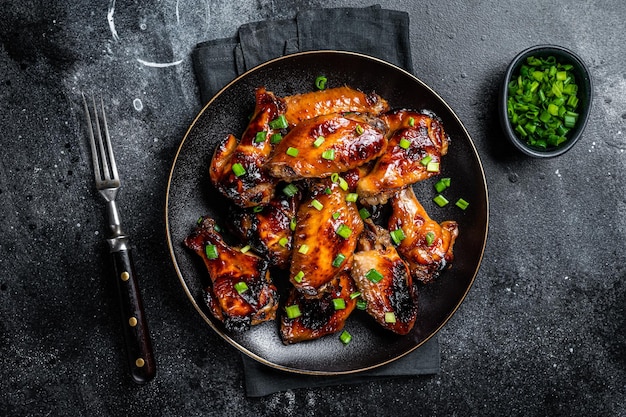 Ailes de poulet cuites au four avec sauce au piment sucré dans une assiette Fond noir Vue du haut