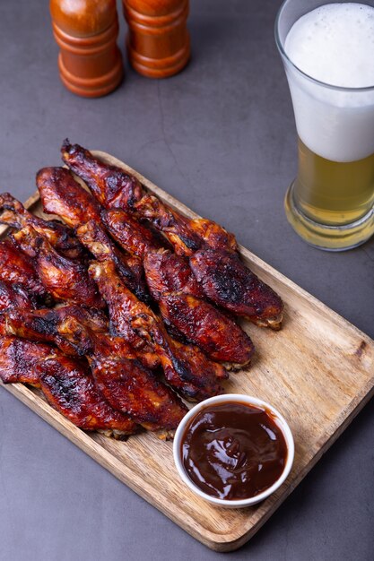 Ailes de poulet frit sur une planche de bois avec sauce barbecue et un verre de bière.