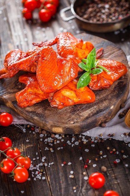 ailes de poulet fumé, épices, légumes sur une planche à découper de cuisine, sombre et de mauvaise humeur, clouseup