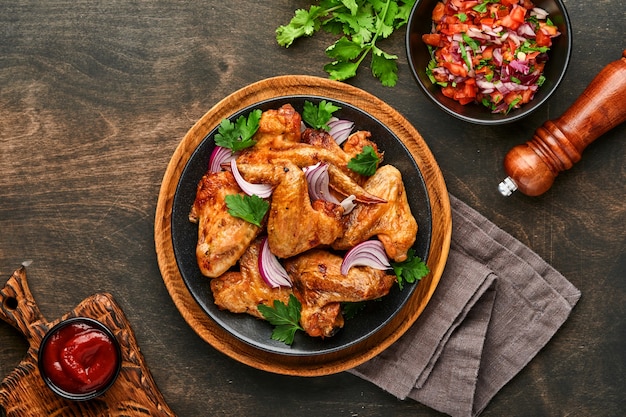 Ailes de poulet grillées ou barbecue rôti aux épices et sauce tomate salsa sur une plaque noire. Vue de dessus avec espace de copie.