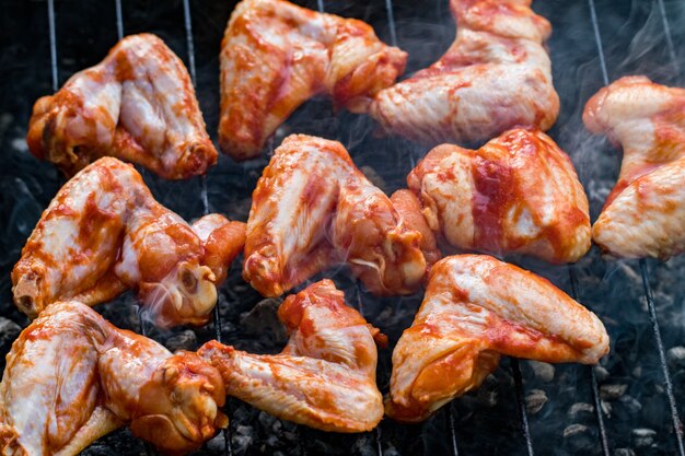 Ailes de poulet marinées épicées grillées sur un barbecue d'été avec des flammes chaudes en vue rapprochée.