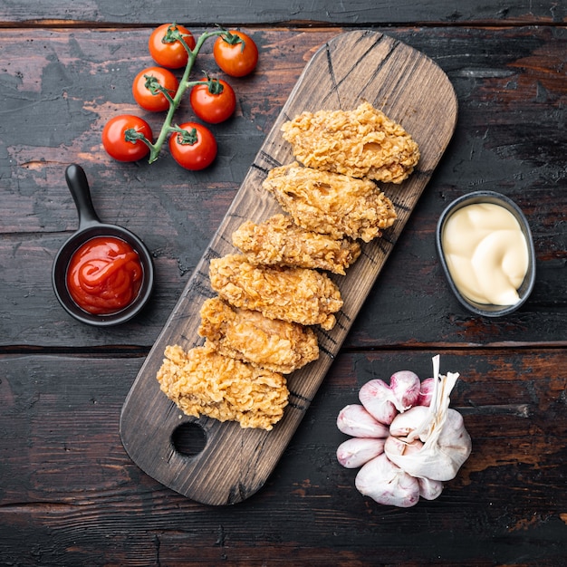 Ailes de poulet panées coupées sur une vieille table en bois sombre, vue de dessus.