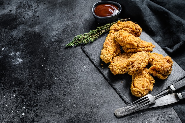 Ailes de poulet panées frites épicées. Fond noir.