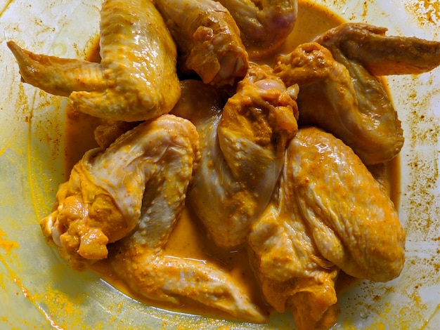 Les ailes de poulet sont dans un bol avec de la poudre de curcuma