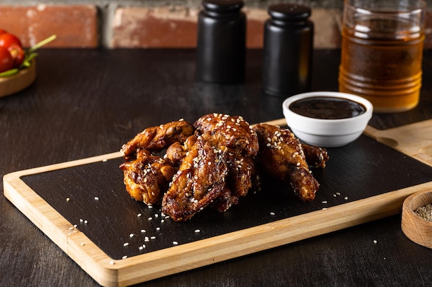 Ailes de poulet teriyaki grillées au sésame sur une planche à découper sombre sur fond bois foncé