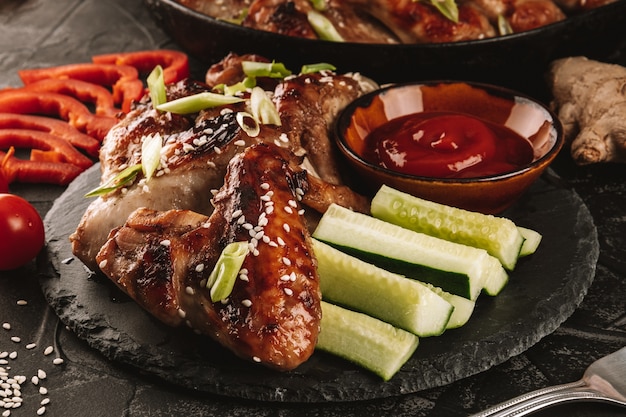 Ailes de poulet teriyaki avec sauce et légumes sur une plaque d'ardoise noire