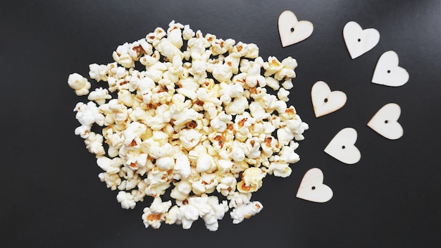 Aime le concept de pop-corn. Photo horizontale. Aliments sucrés. Pop-corn salé classique avec des coeurs en bois sur une surface noire