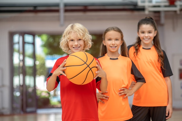 Aime jouer. Les enfants en tenue de sport debout avec un ballon et à la recherche apprécié