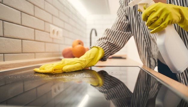 Photo aime ma maison. jeune femme étant à la maison et essuyant la surface en verre sur le four