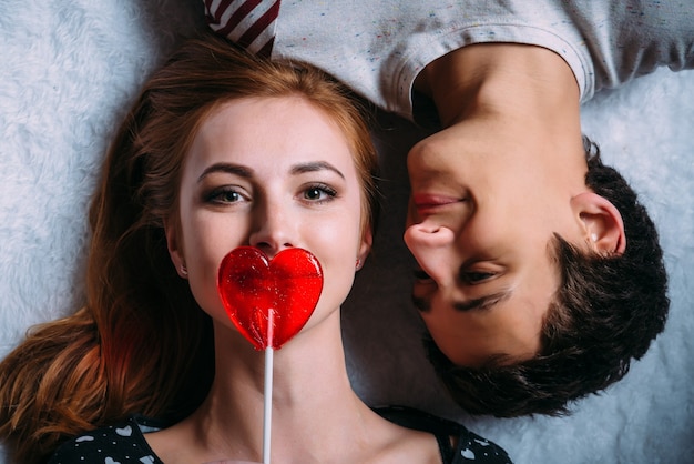 Photo aimer couple allongé sur le sol fille couvre sa bouche avec une sucette