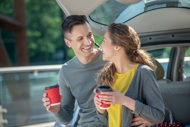Aimer l'homme et la femme buvant du café près de la voiture