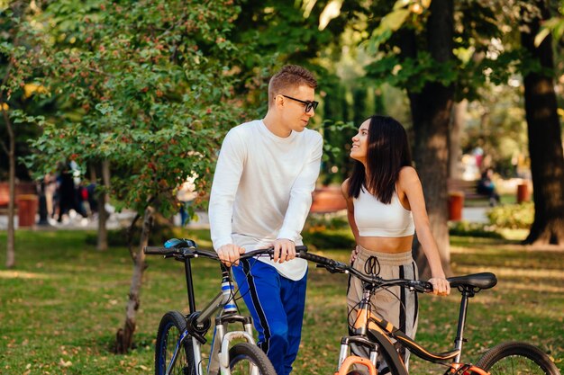 Aimer le jeune couple debout dans un parc d'automne avec des vélos et parler avec un sourire