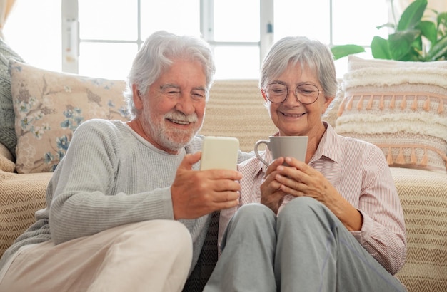 Aimer le vieux couple de famille senior assis sur le sol à la maison en regardant le smartphone ensemble romantique