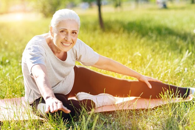 Aimez ce que vous faites. Heureux souriant senior woman stretching et assis sur le tapis roulant