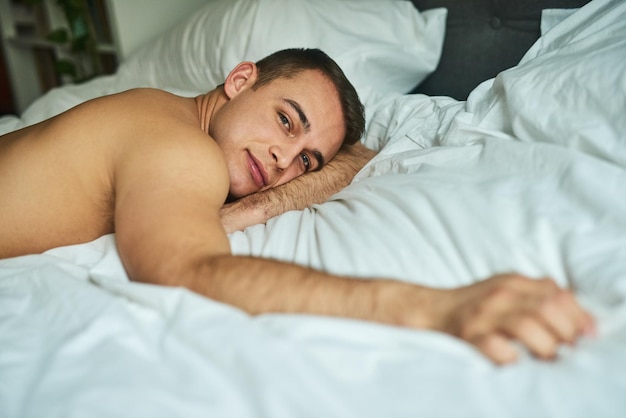 L'air en forme entre les draps Photo recadrée d'un jeune bel homme allongé dans son lit à la maison