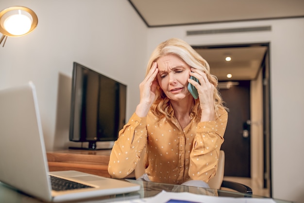 L'air stressé. Jolie femme blonde assise parlant au téléphone et ayant l'air stressée