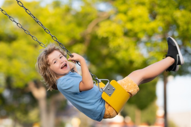 Aire de jeux extérieure drôle enfant sur balançoire petit garçon se balançant sur l'aire de jeux heureux mignon enfant excité sur