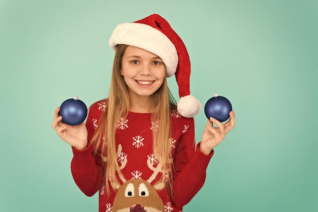 Ajouter plus de décorations Impliquer l'enfant dans la décoration Décorer l'arbre de Noël Fille sourire visage tenir des boules ornements fond bleu Laissez l'enfant décorer l'arbre de Noël partie préférée de la décoration