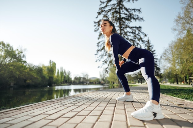 Ajuster la jeune fille en vêtements de sport bleu foncé exerçant dans le parc