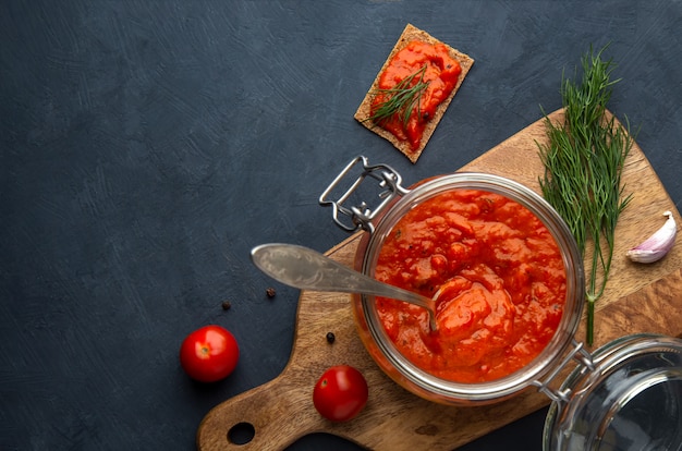 Photo ajvar, pinjur, lutenitsa, harissa dans la banque sur un espace sombre