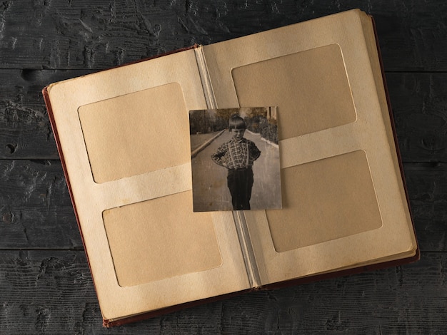 Un album photo ouvert avec une photo d'un garçon sur une table en bois. Ancienne photo élégante. Histoire.