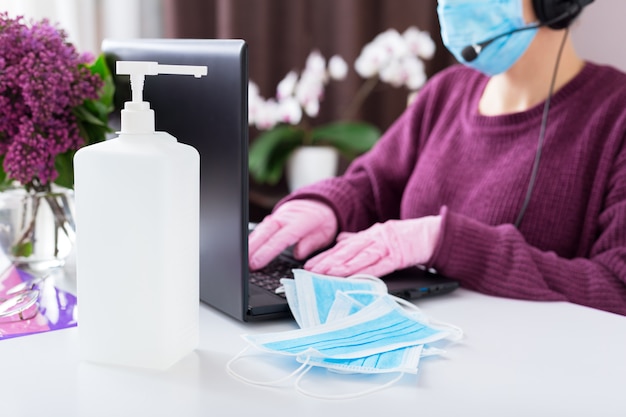 Alcool désinfectant gel hygiène des mains, masques bleus chirurgicaux médicaux. Coronavirus Covid-19. Femme travaille en ligne à la maison sur un ordinateur portable.Travail à distance.Appel vidéo, pigiste joueur, éducation en ligne, soutien