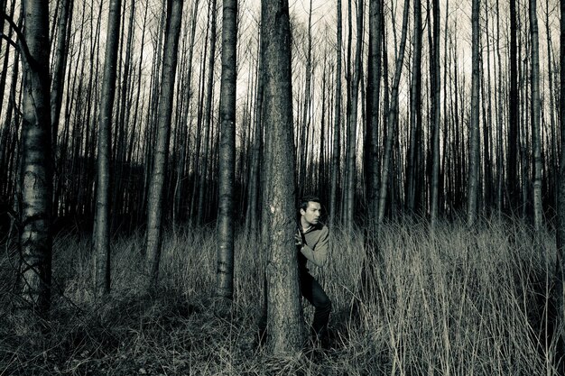 Photo alerte homme debout derrière l'arbre dans la forêt contre le ciel