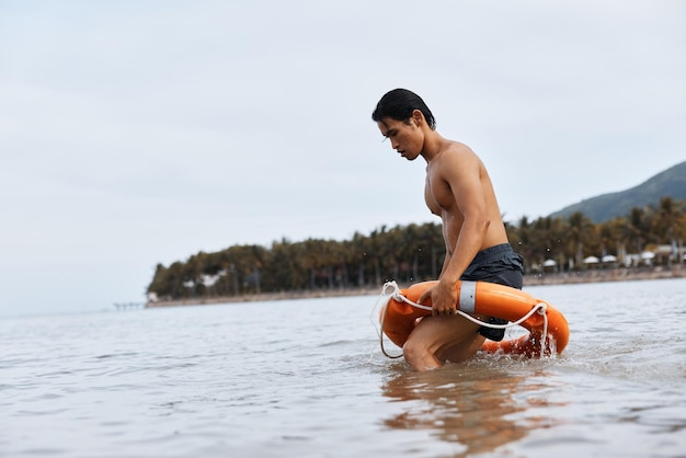 Alerte de sécurité d'été sauveteur asiatique sauvant un homme sur la plage assurant des vacances heureuses à la station balnéaire