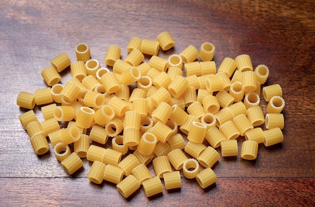 ALIMENT - pâtes italiennes non cuites dans de petits tubes à nervures sur une table en bois