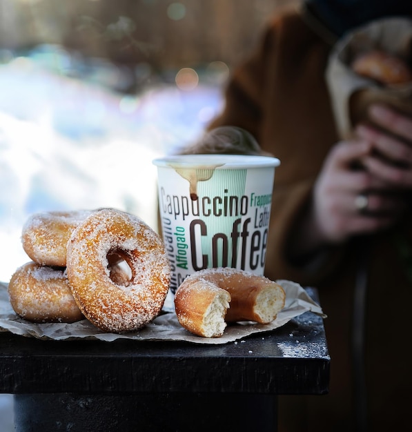 L'alimentation de rue. Beignets, tasse de café chaud en papier sur fond de parc d'hiver enneigé.